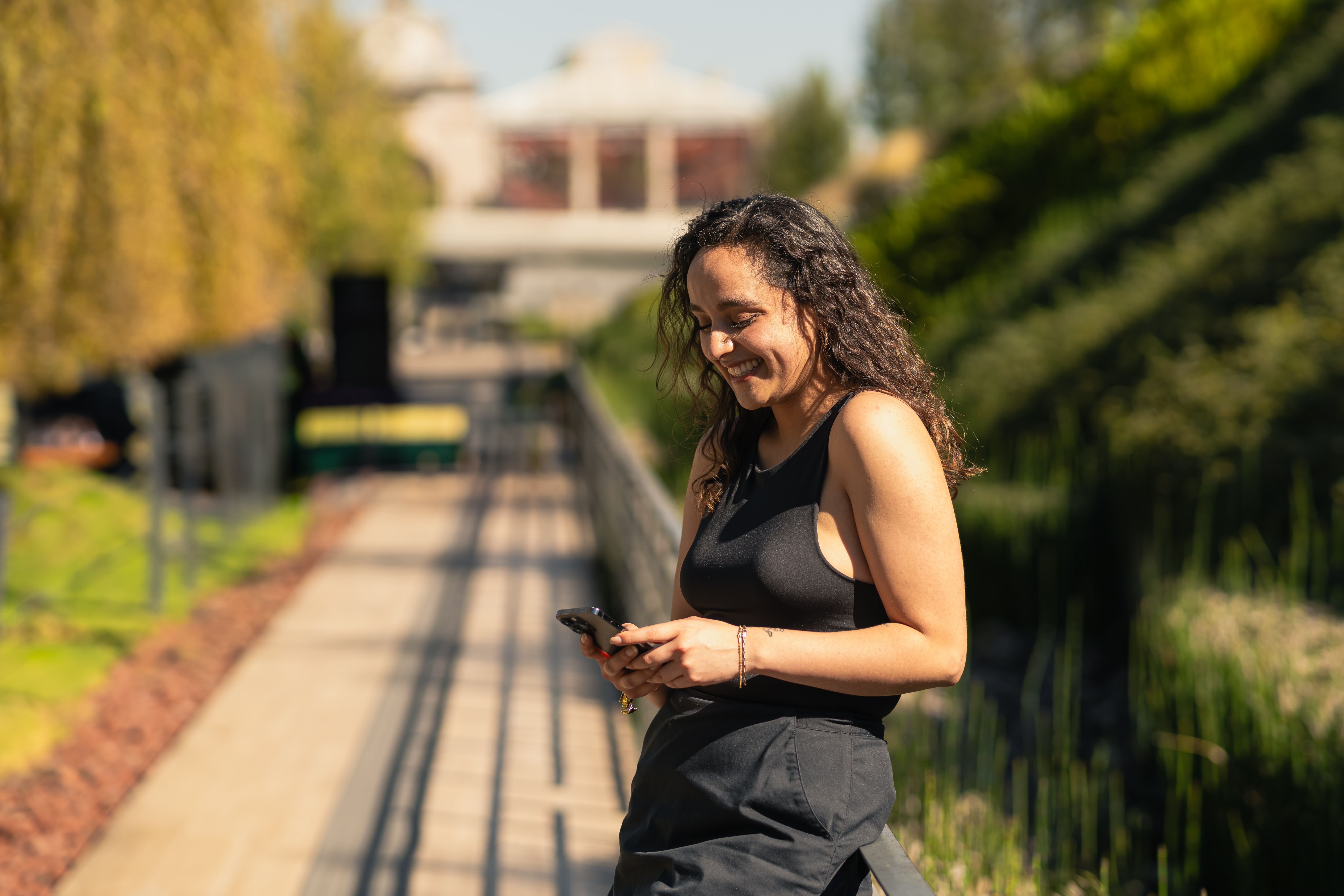 Une jeune femme sourit en écrivant sur son téléphone dans un parc