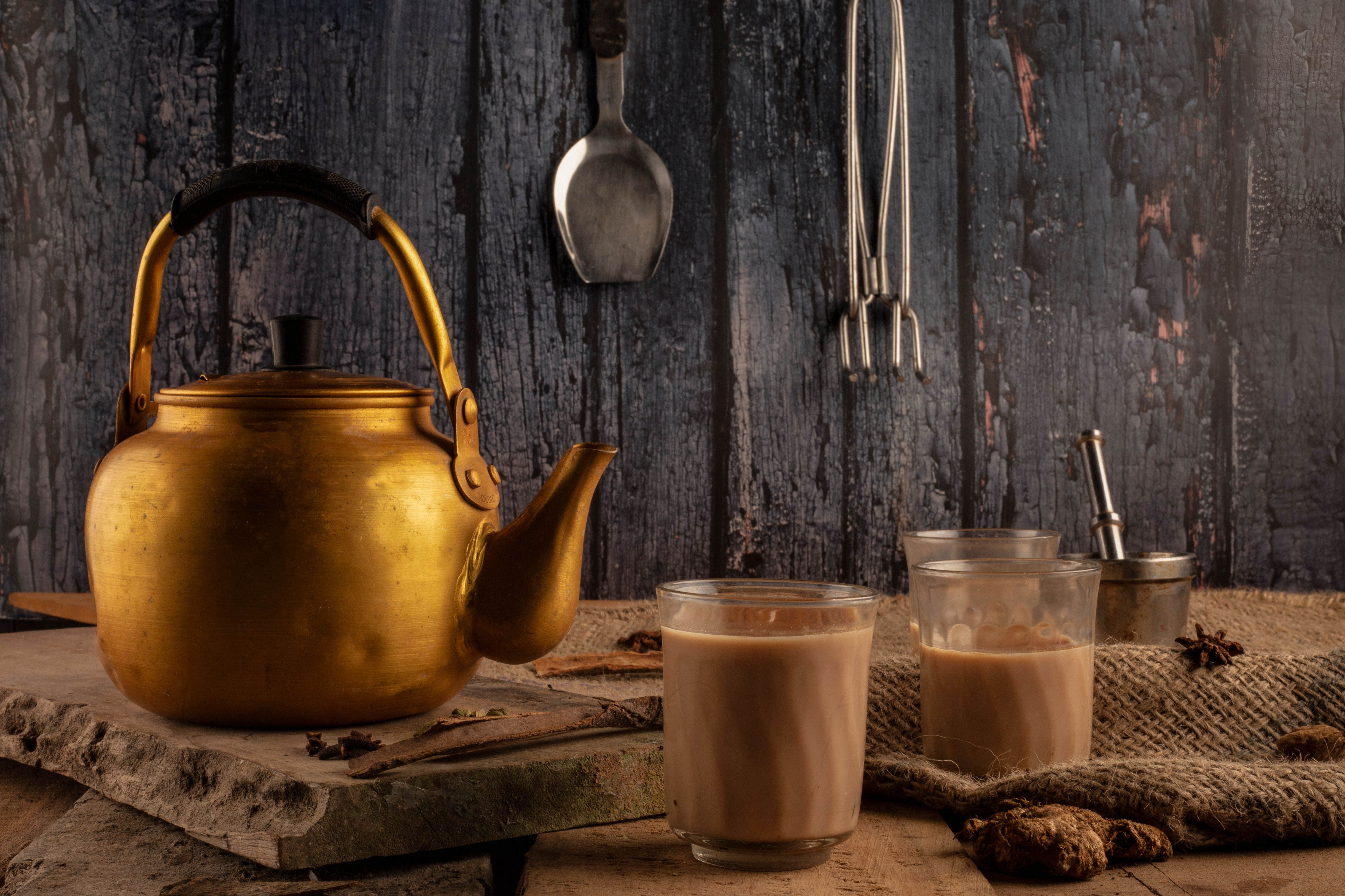 A brass kettle and glasses of chai on a table